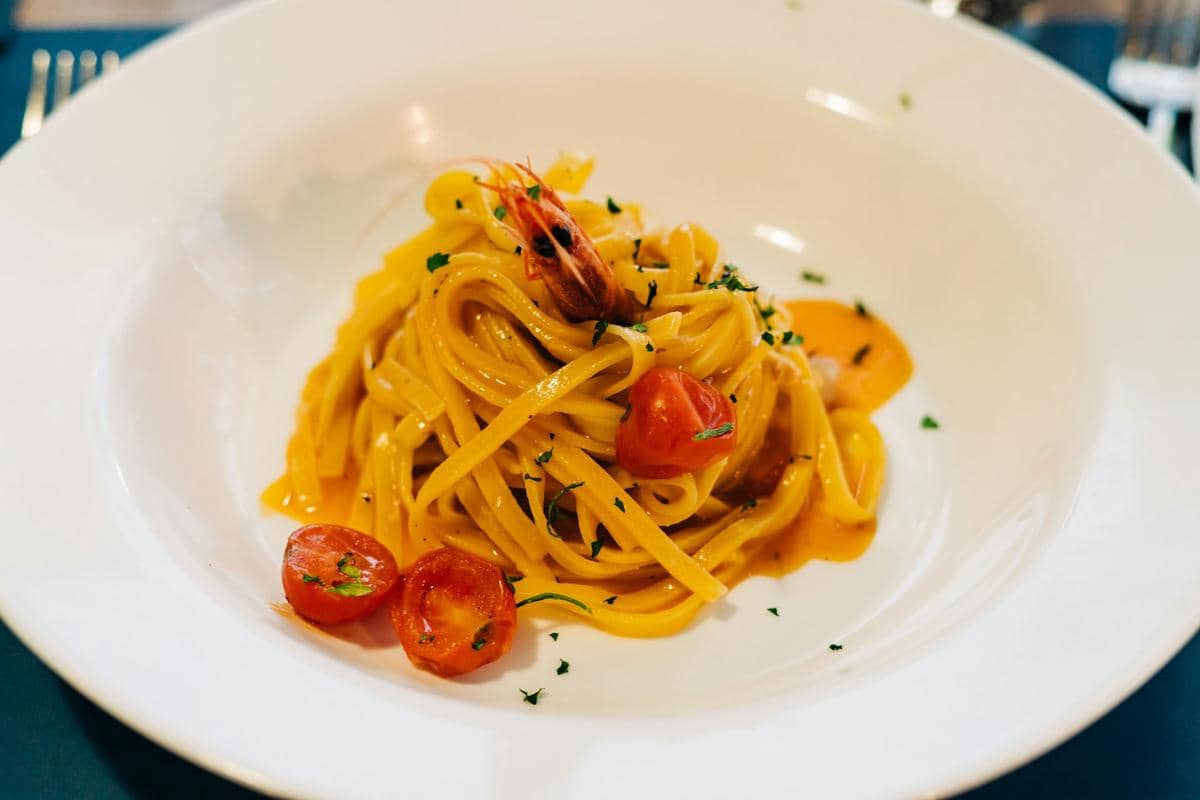 Sepiring pasta berwarna kuning dengan saus mentega dan saffron, disajikan sederhana sebagai ilustrasi hidangan.