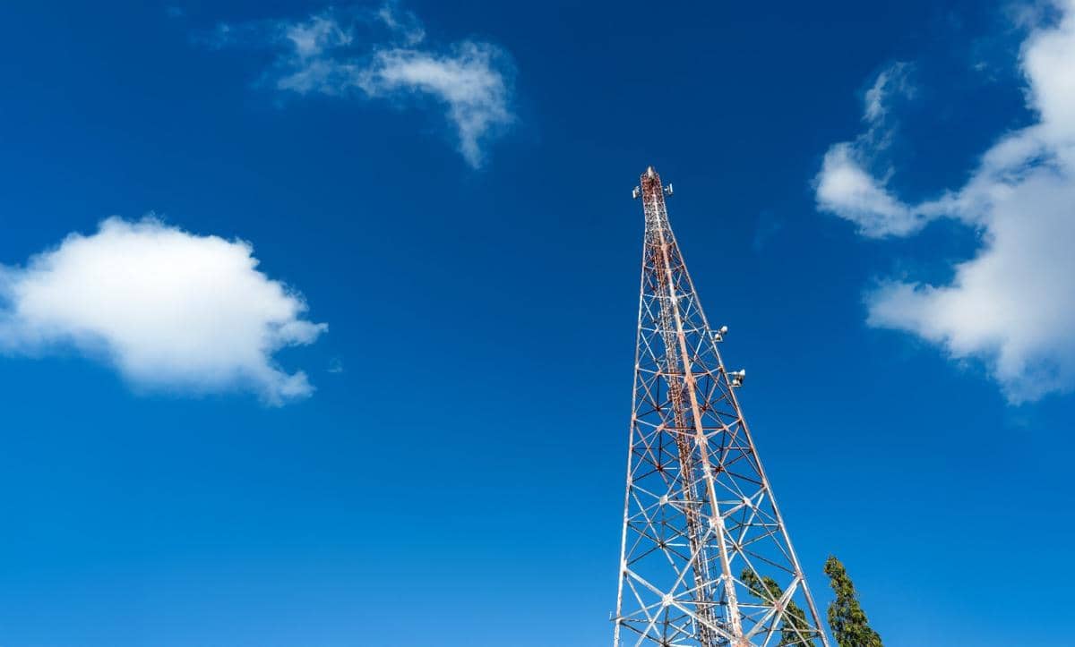 Ilustrasi menara BTS Indosat dengan struktur rangka baja menjulang dan perangkat antena telekomunikasi di bagian puncak.