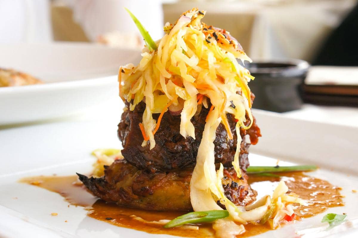 Steak hache berlapis saus lada cokelat disajikan di piring putih bersama kentang goreng dan hiasan sayuran.
