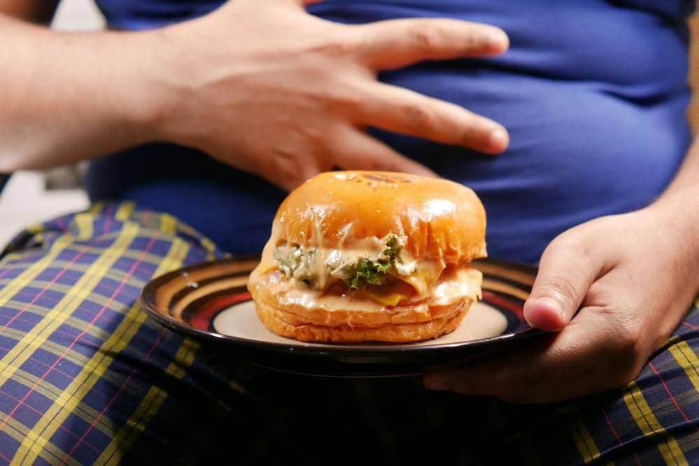 Seorang dengan berat badan berlebih sedang makan burger 