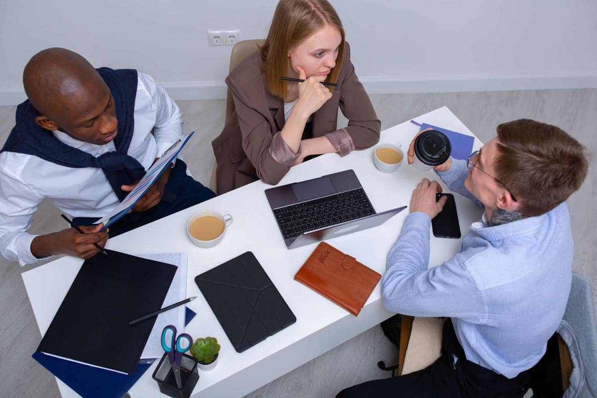 Dua rekan kerja berbincang di kantor, menggambarkan kebiasaan bergosip dengan teman kerja saat waktu senggang.