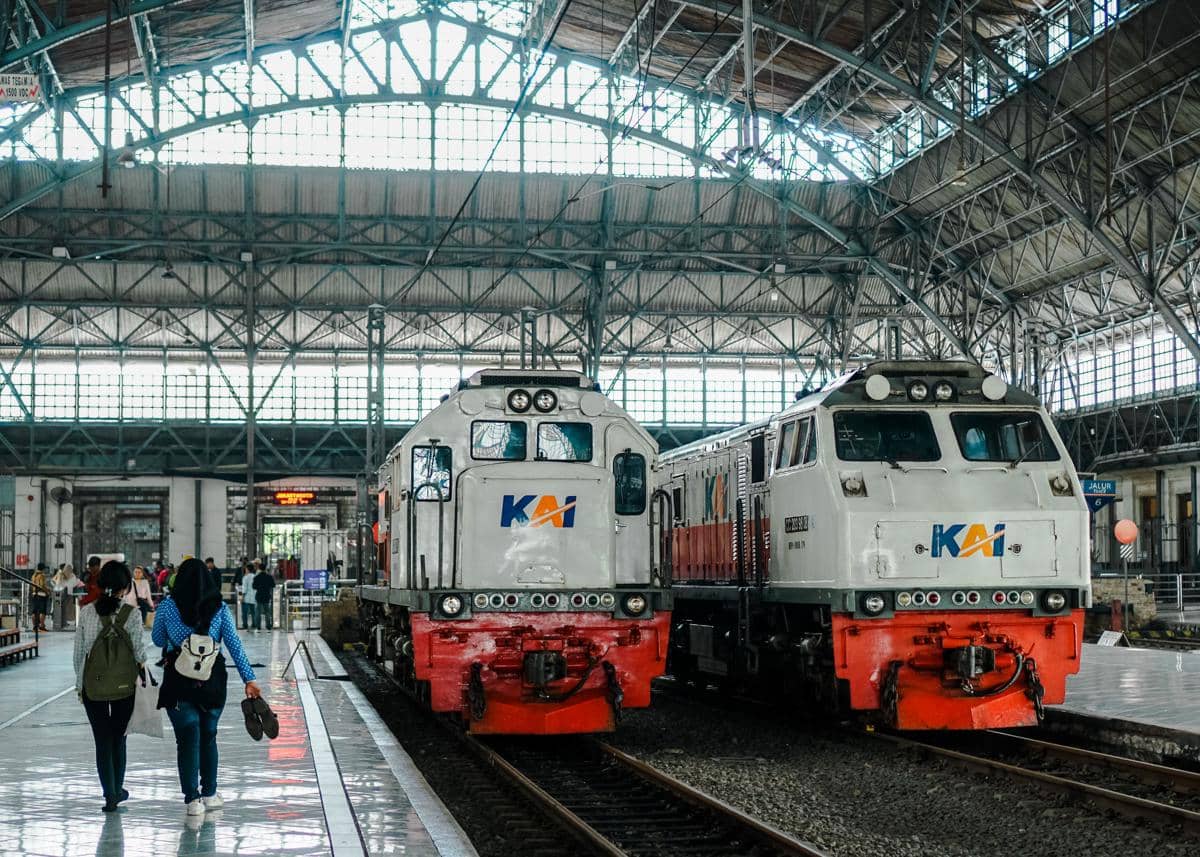 Dua lokomotif KAI berada di peron stasiun dengan penumpang berjalan di area stasiun