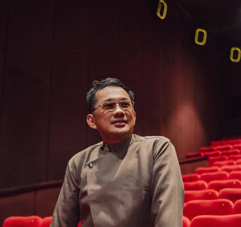 Potret Hanung Bramantyo dengan ekspresi tenang, mengenakan pakaian gelap dan memandang ke arah kamera.