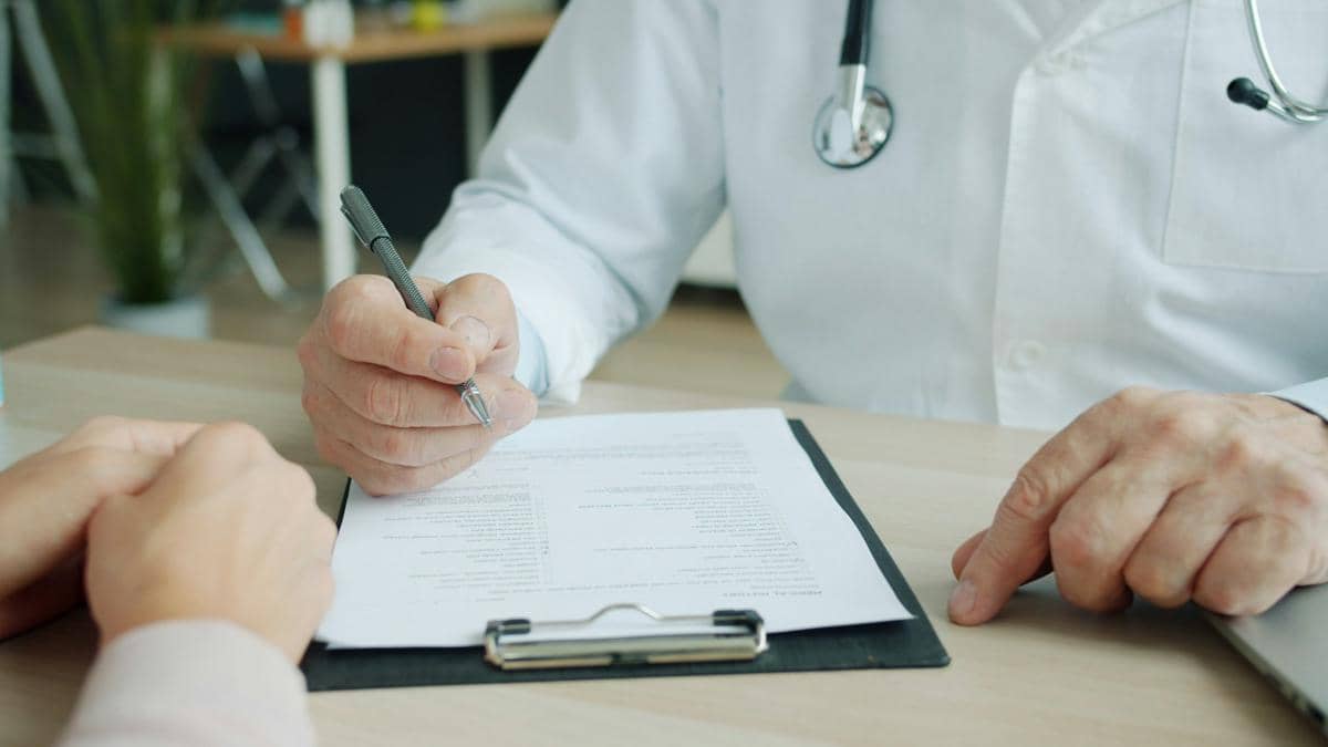 Dokter memegang pena dan menunjuk lembar pemeriksaan saat berkonsultasi dengan pasien