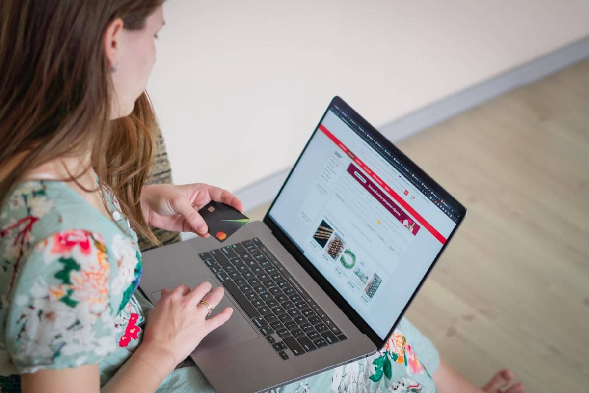 Seseorang berbelanja online melalui laptop sambil memegang kartu pembayaran.