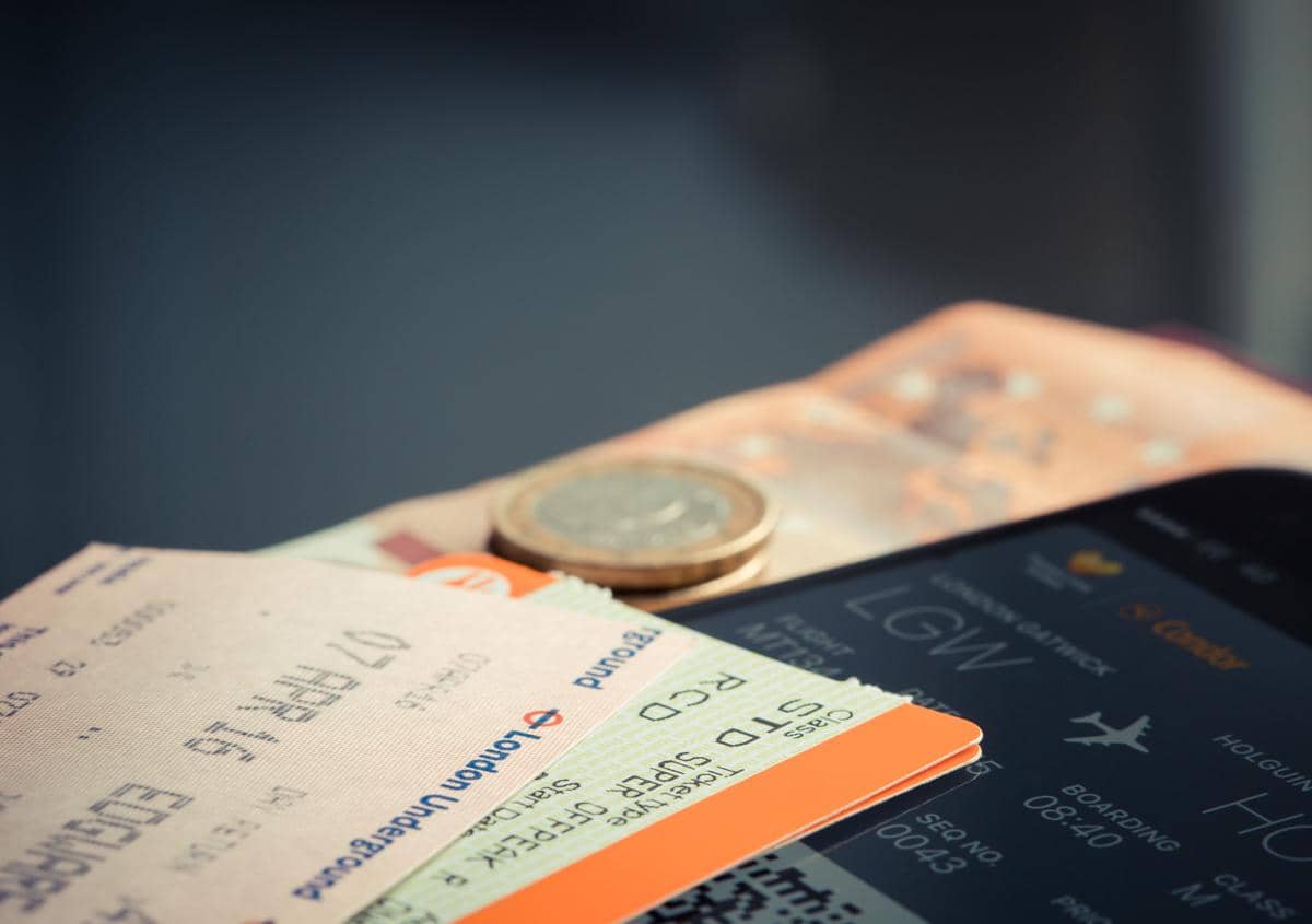 Tiket pesawat, uang kertas, koin, dan ponsel di atas meja.