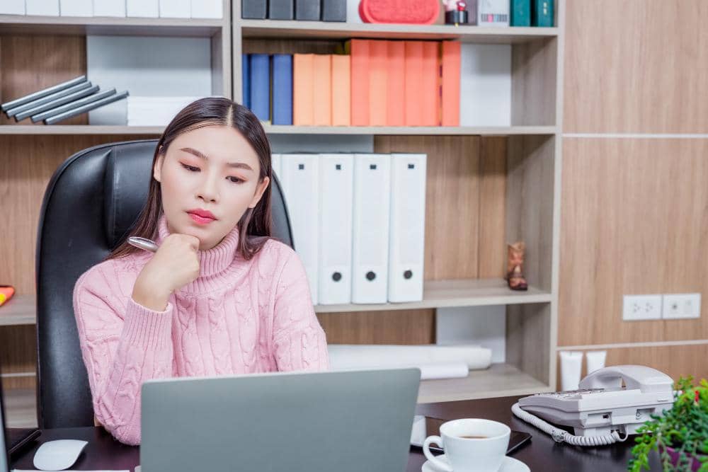 Ilustrasi perempuan duduk di depan laptop dengan ekspresi lelah, menggambarkan hilangnya kreativitas saat bekerja.