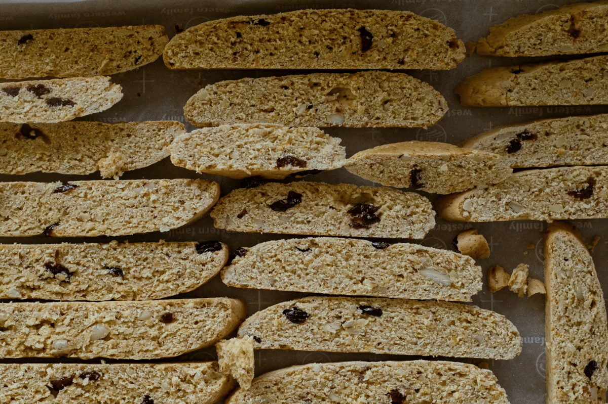 Ilustrasi biscotti, kue kering Italia berbentuk panjang berwarna cokelat keemasan, tersusun di atas permukaan terang.