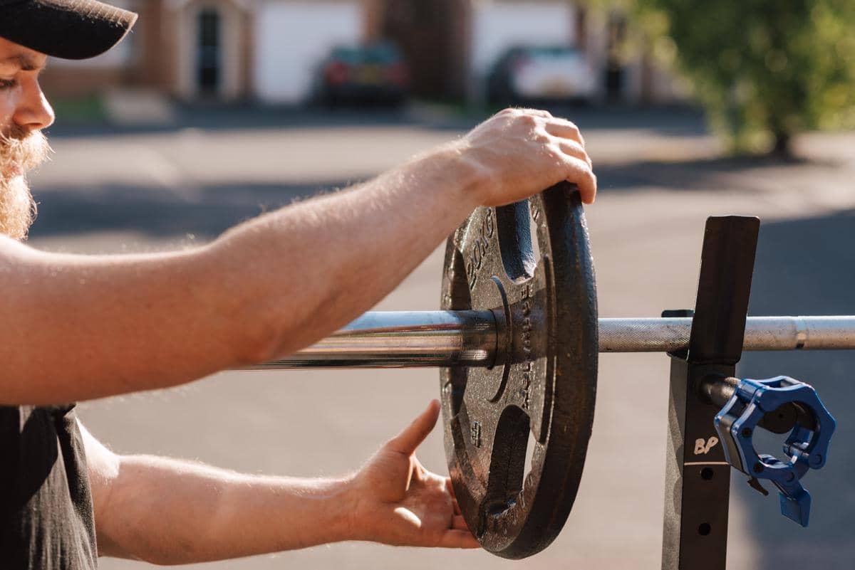seorang pria sedang menambah piringan beban ke barbell untuk menerapkan progressive overload