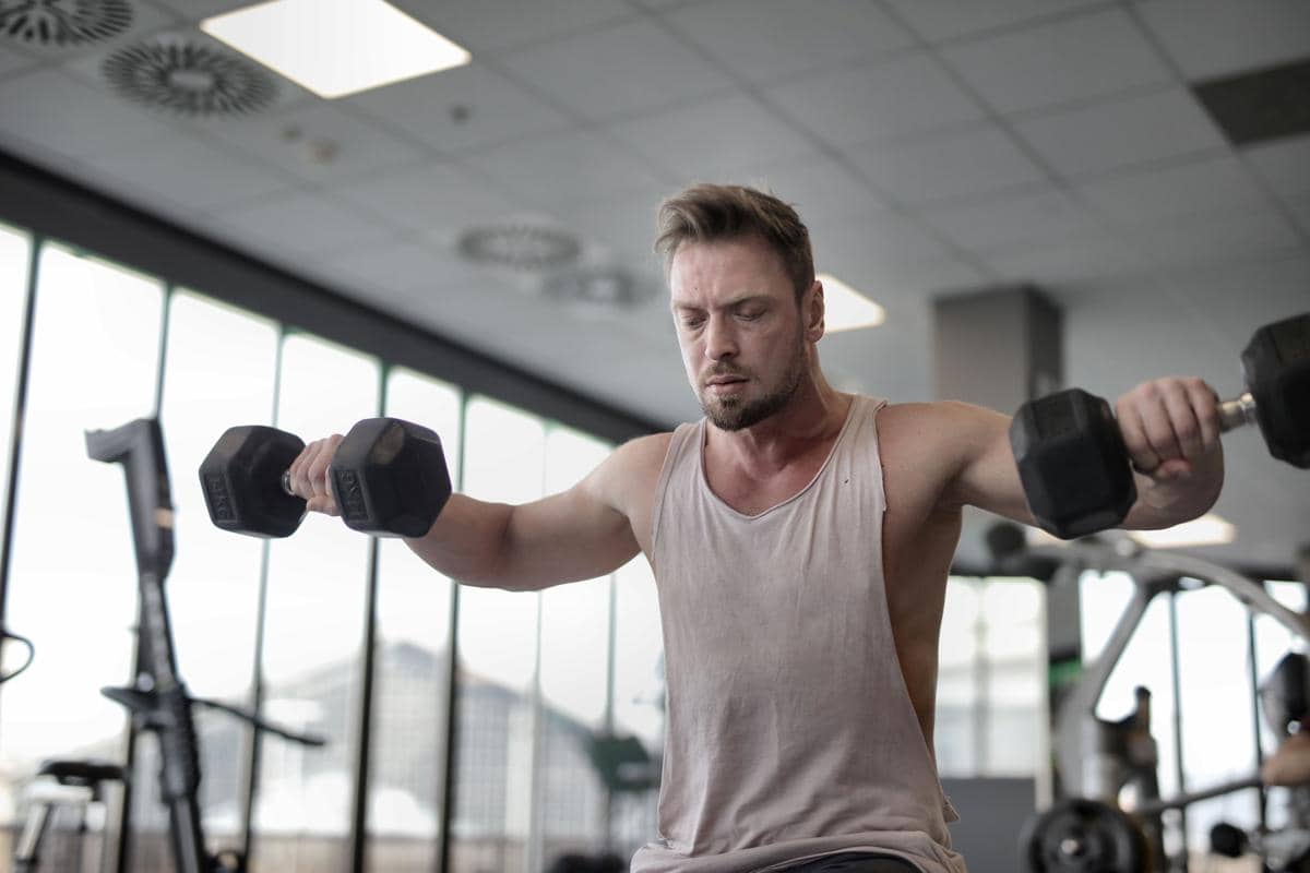 seorang pria sedang melakukan gerakan pengulangan reps dengan beban dumbbell di tempat gym