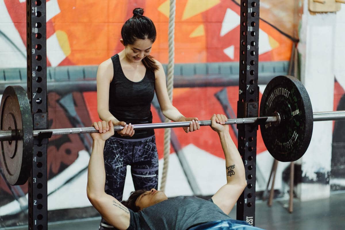 seorang wanita menjadi spotter yang memandu dan menjaga keselamatan teman pria saat latihan bench press