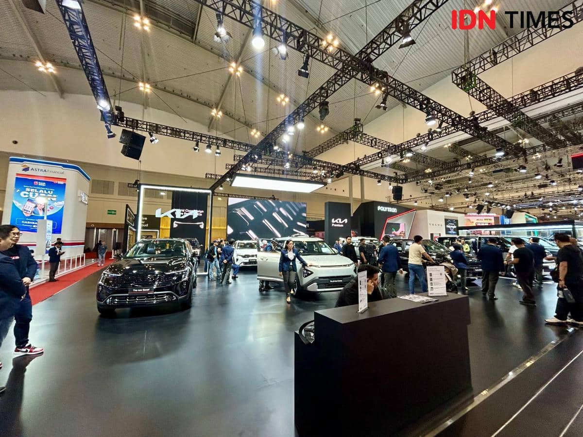 Booth Kia dengan logo merek otomotif, area pameran kendaraan, dan pencahayaan terang di dalam ruangan.