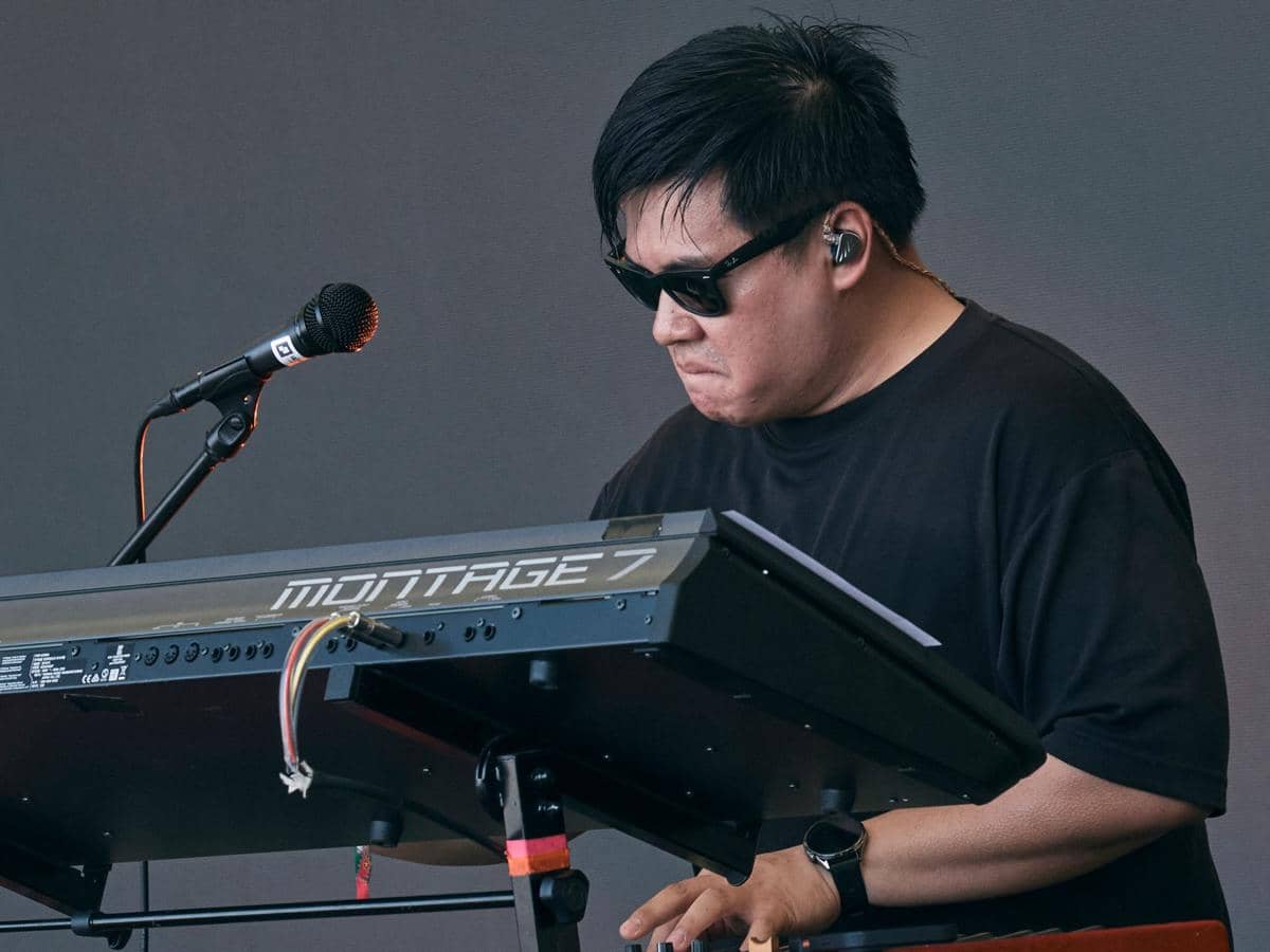 Potret Kenan Loui Wijaya mengenakan kaus putih sambil tersenyum ke arah kamera dengan latar ruangan gelap.