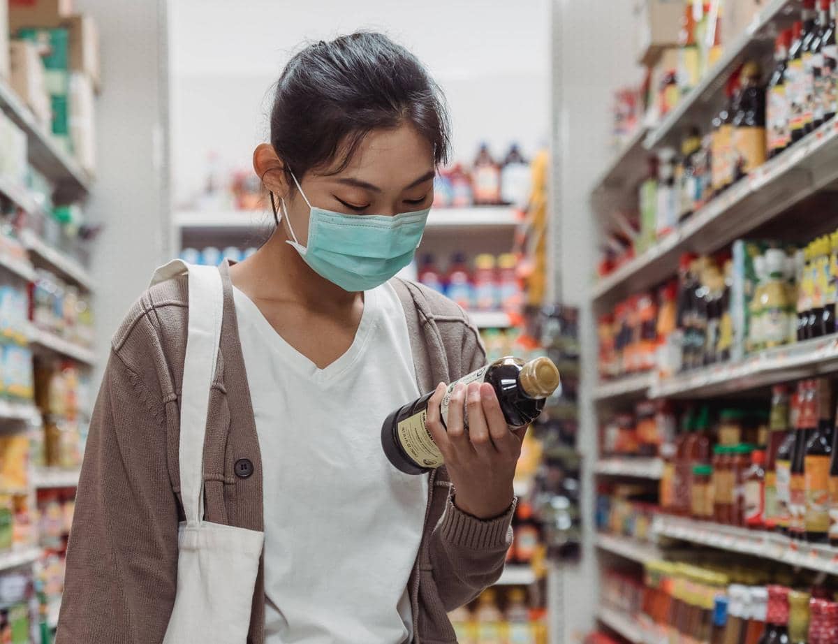 Seseorang membaca label pada kemasan makanan sebagai ilustrasi pentingnya memeriksa informasi produk sebelum membeli.