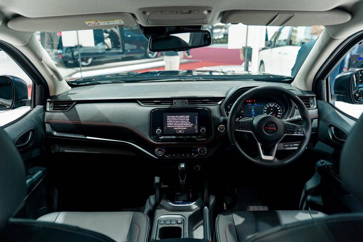 Interior Nissan Navara PRO-4X dengan dasbor, layar infotainment, setir, panel instrumen, dan konsol tengah bernuansa gelap.
