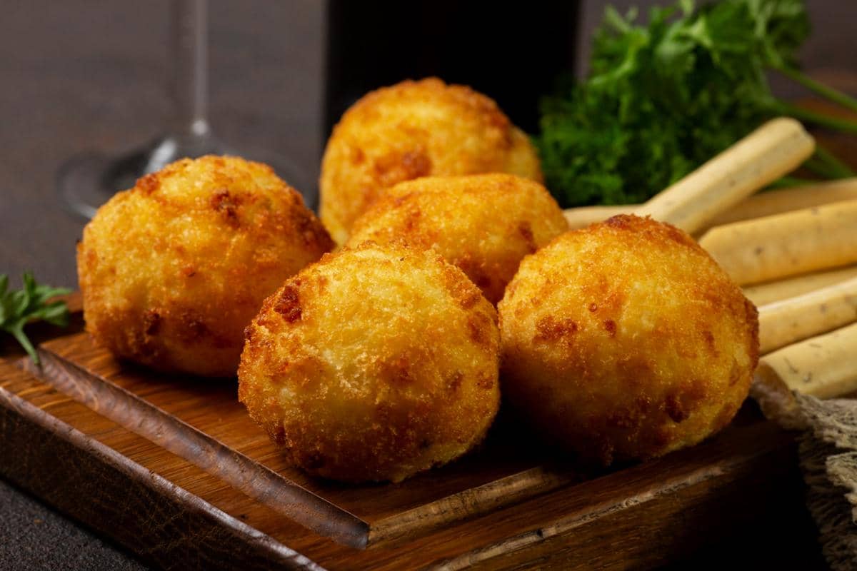 Ilustrasi arancini, bola nasi khas Italia berlapis tepung roti dengan isian keju meleleh yang disajikan di piring.