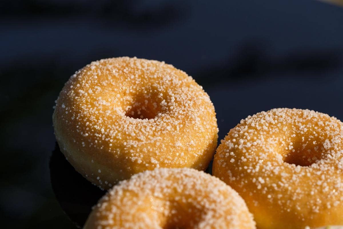 Ilustrasi donat dengan lapisan gula dan taburan warna-warni sebagai sajian camilan manis di atas latar sederhana.