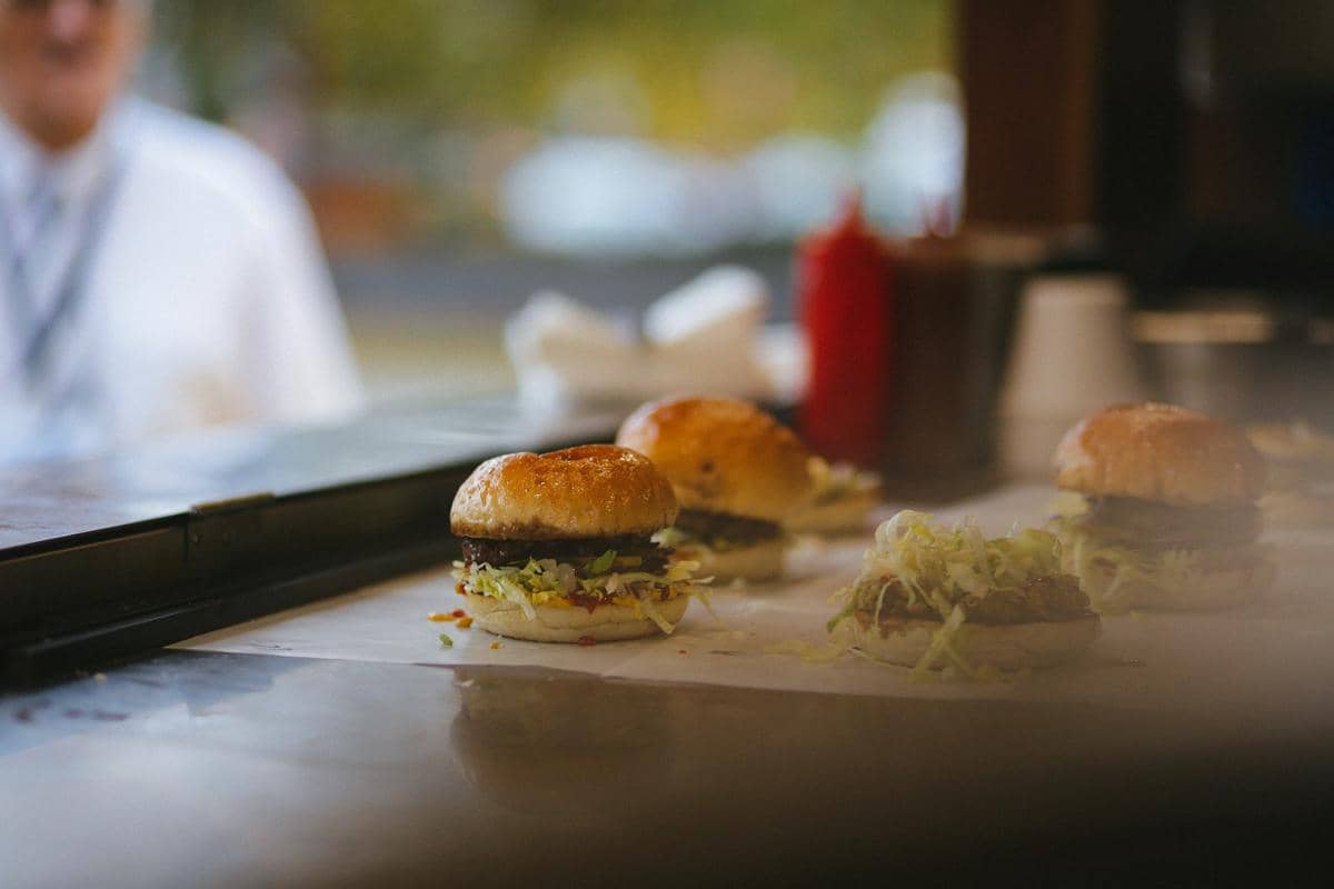 Ilustrasi proses membuat hatch chile burger dengan roti, patty daging, keju, dan cabai hijau sebagai pelengkap.