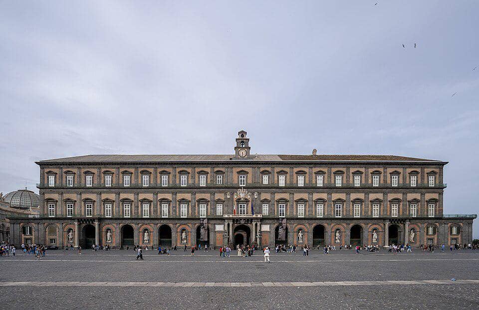 Fasad Royal Palace di Napoli dengan bangunan klasik berwarna cokelat dan halaman terbuka di depannya.