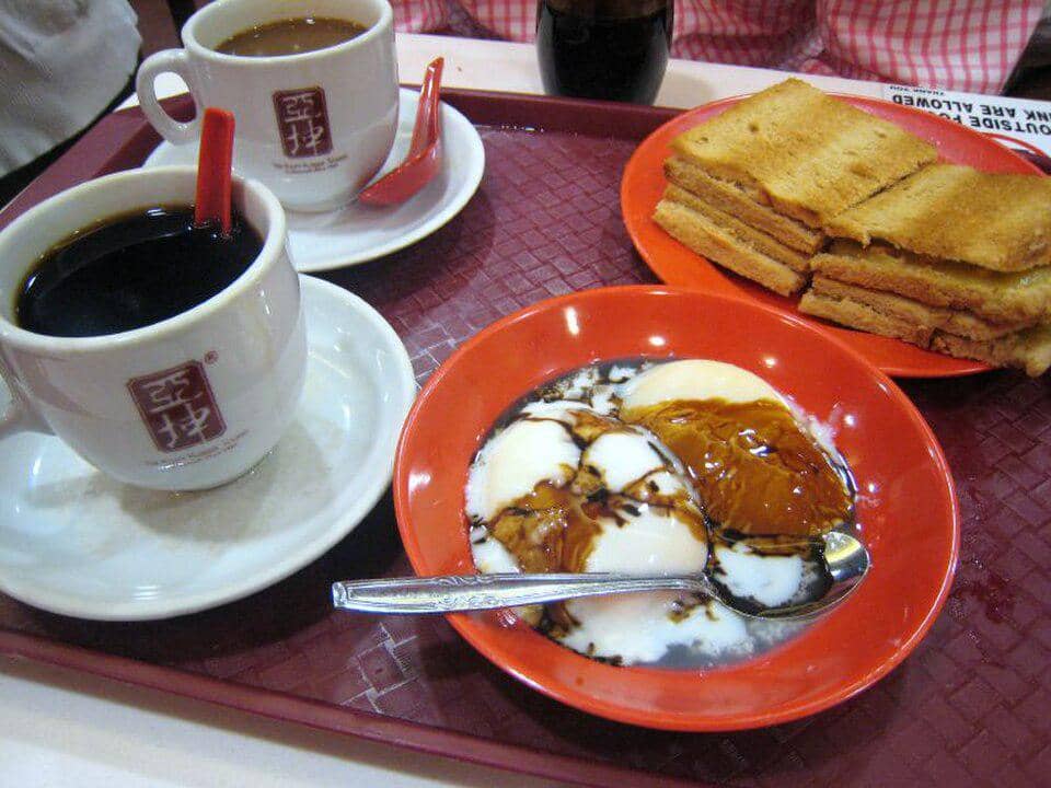 Sepiring kaya toast Ya Kun dengan telur setengah matang dan secangkir kopi, disajikan di atas meja.