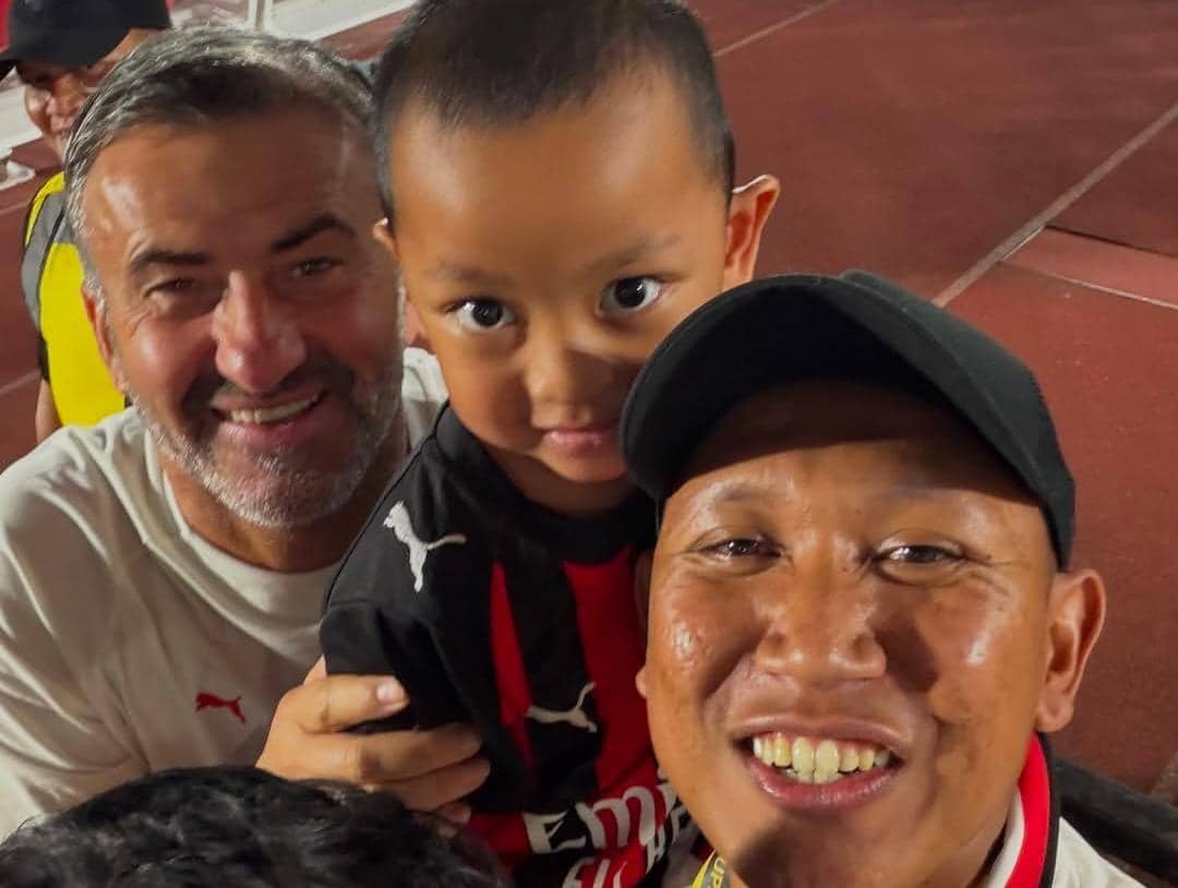 Oki Rengga dan Arthur berfoto bersama pemain AC Milan di lapangan latihan dengan latar fasilitas klub.