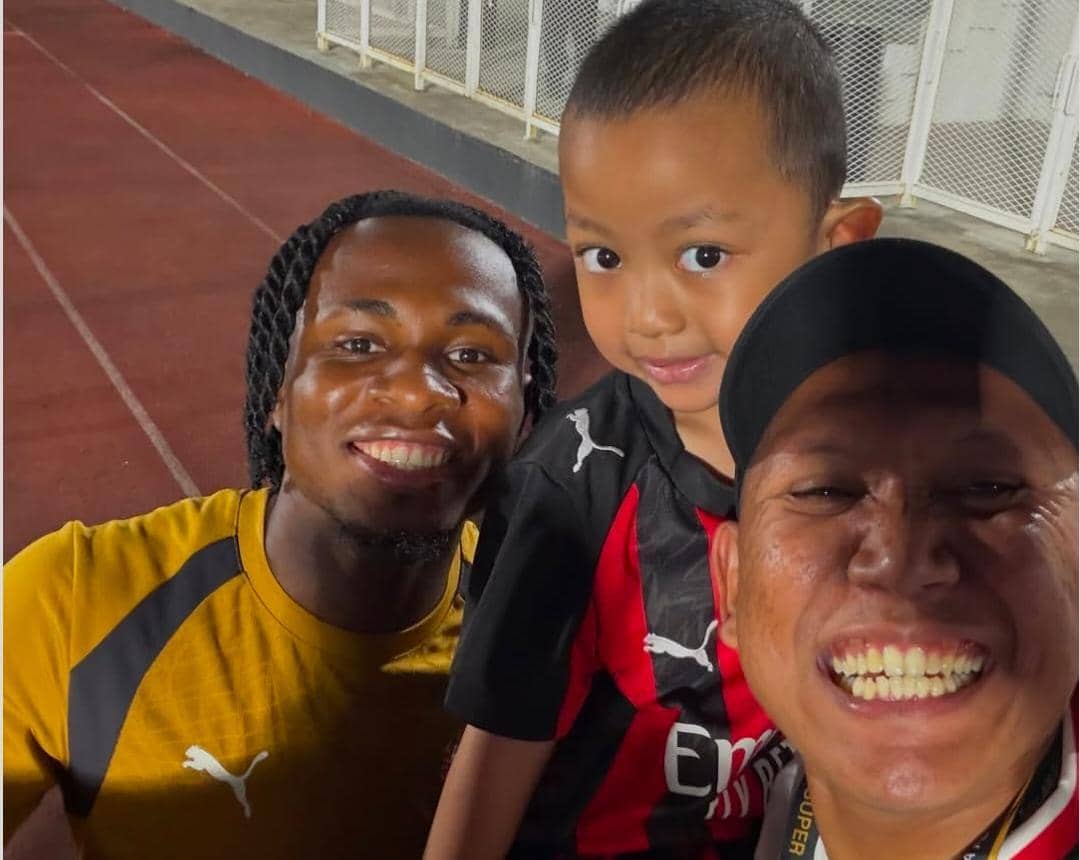 Oki Rengga dan Arthur berpose bersama sejumlah pemain AC Milan di lapangan latihan dengan latar sesi latihan tim.