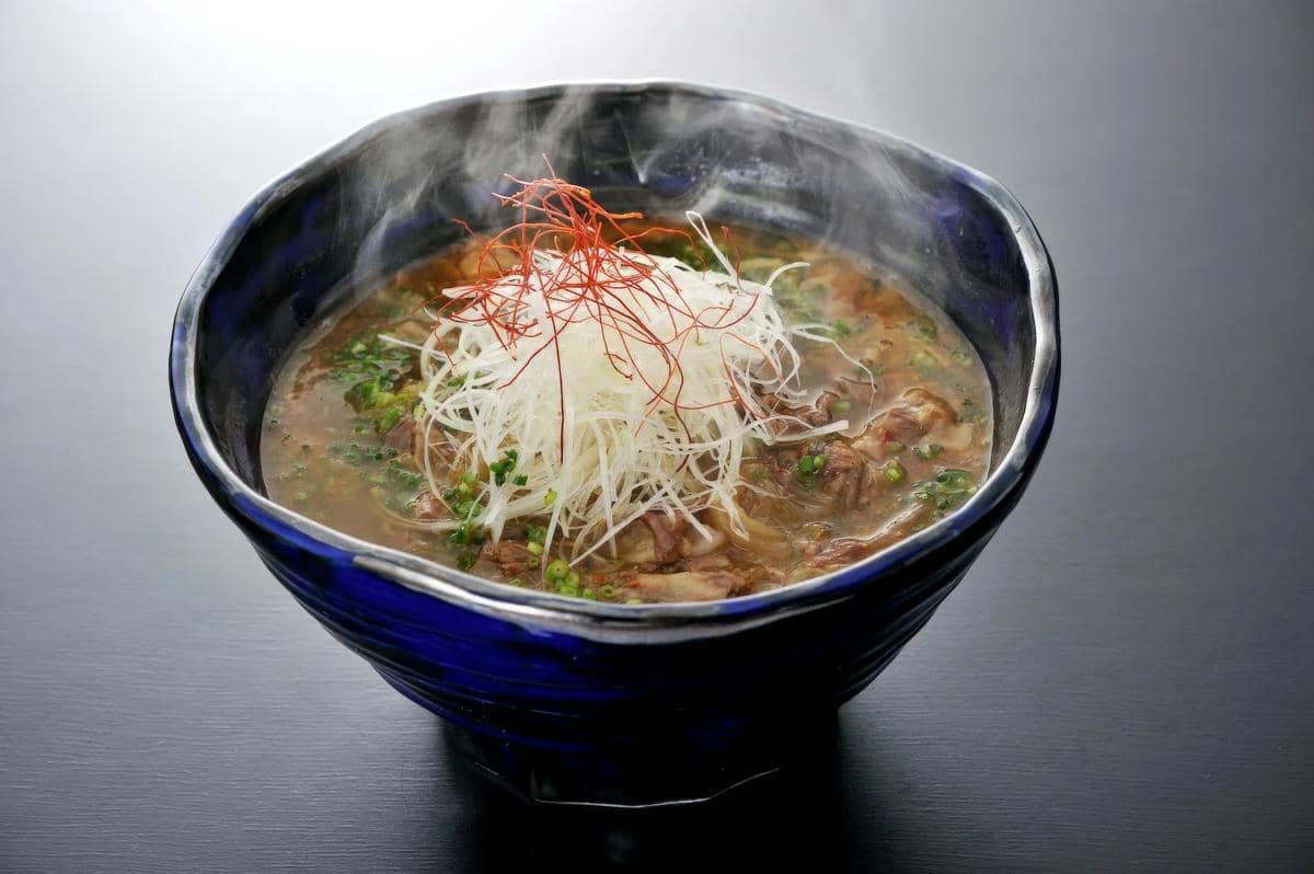 Semangkuk doenjang jjigae, sup rebusan pasta kedelai fermentasi khas Korea, disajikan hangat sebagai ilustrasi hidangan.