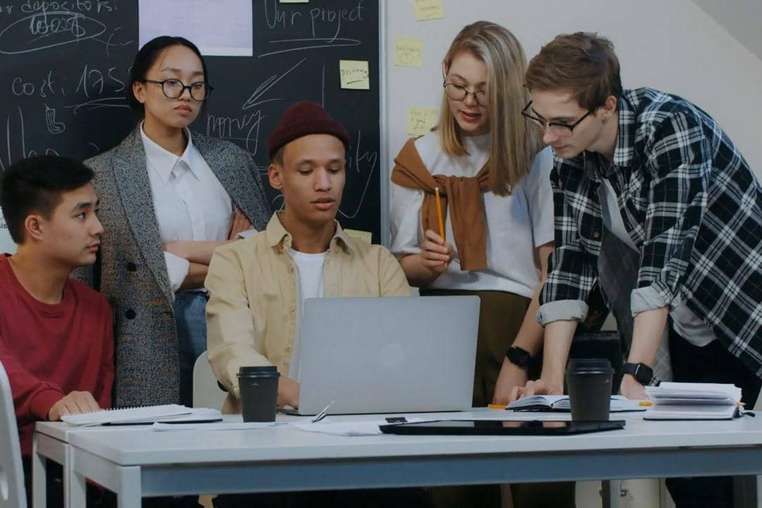 Sekelompok profesional muda sedang berdiskusi di depan laptop saat rapat di kantor.