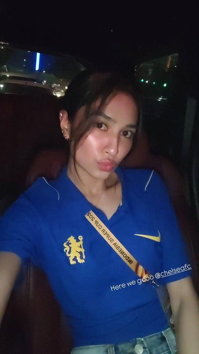 Seorang perempuan berambut panjang mengenakan jersey Chelsea berpose di Stadion Utama GBK saat menyaksikan laga.
