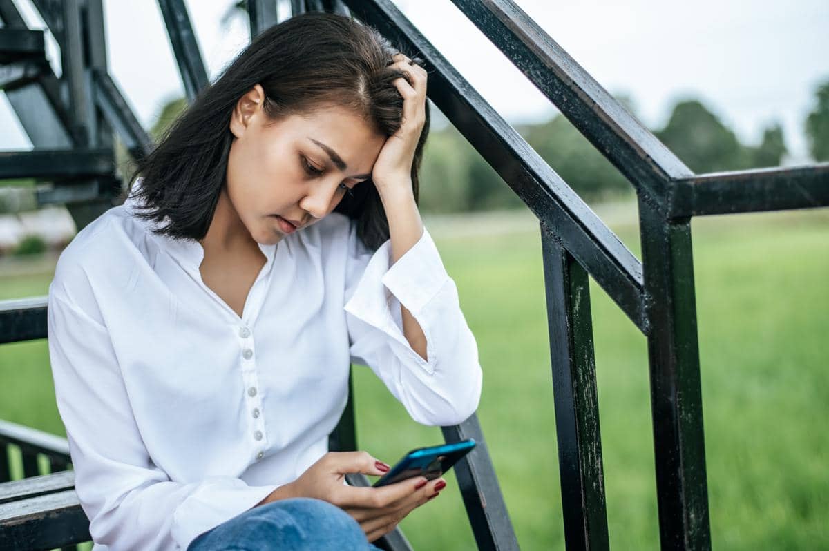 Seorang remaja memgang handphone yg sedang duduk di tangga terlihat stress