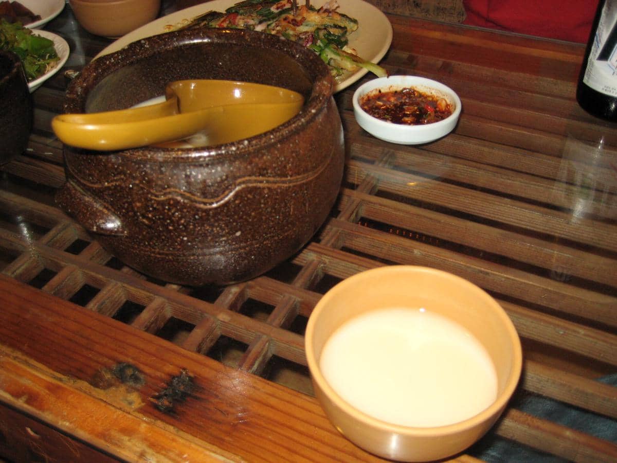 Ilustrasi dongdongju, minuman beras tradisional Korea berwarna putih susu dalam wadah saji bergaya sederhana.