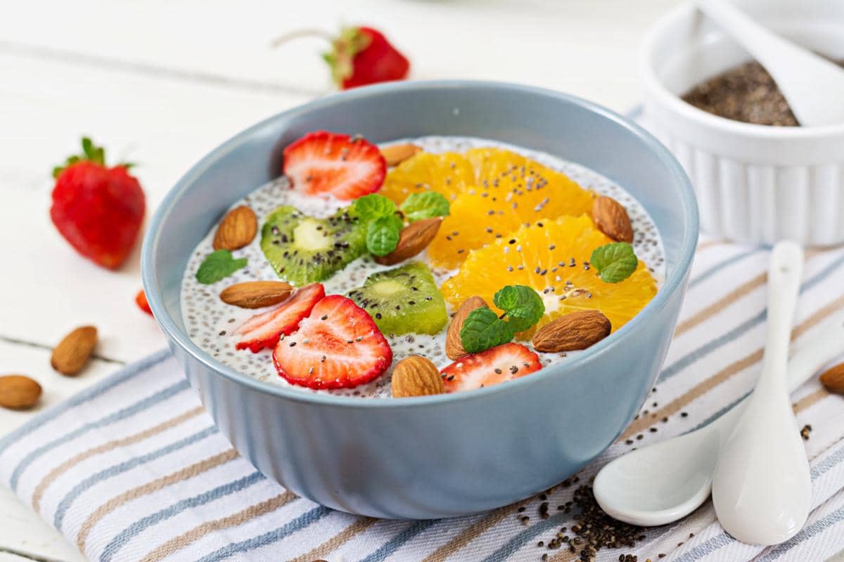 Ilustrasi smoothie bowl dalam mangkuk dengan aneka topping buah, biji-bijian, dan daun sebagai hiasan.