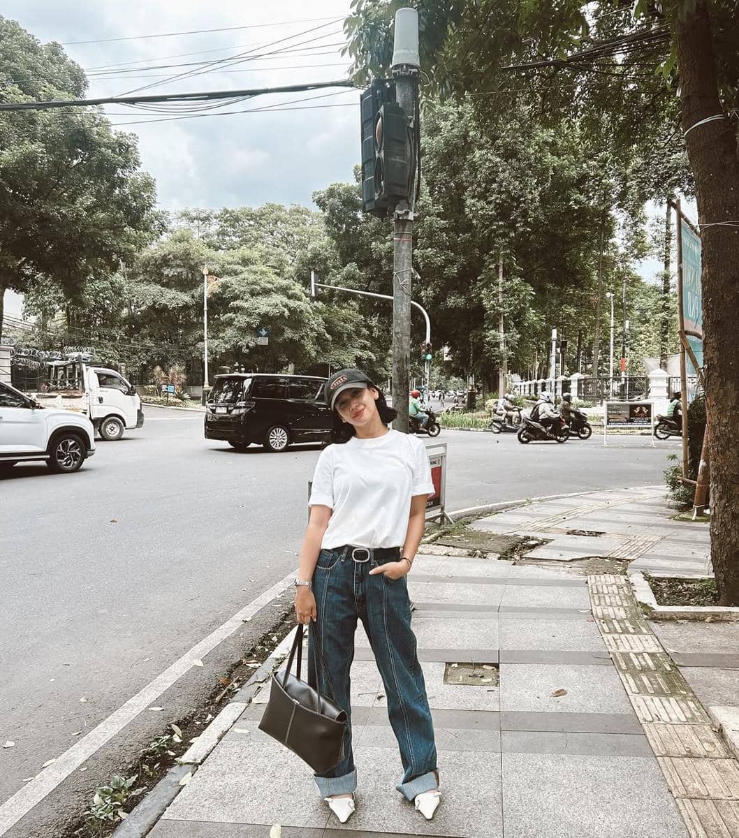 Dea Annisa mengenakan kaus putih polos dan celana jeans biru dalam gaya kasual di luar ruangan.