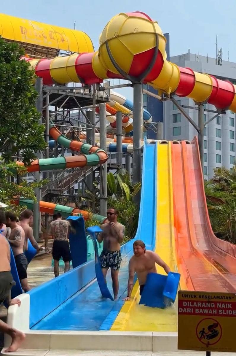 Potret band Neck Deep saat berada di Atlantis Ancol, dengan latar area taman rekreasi di belakang mereka.