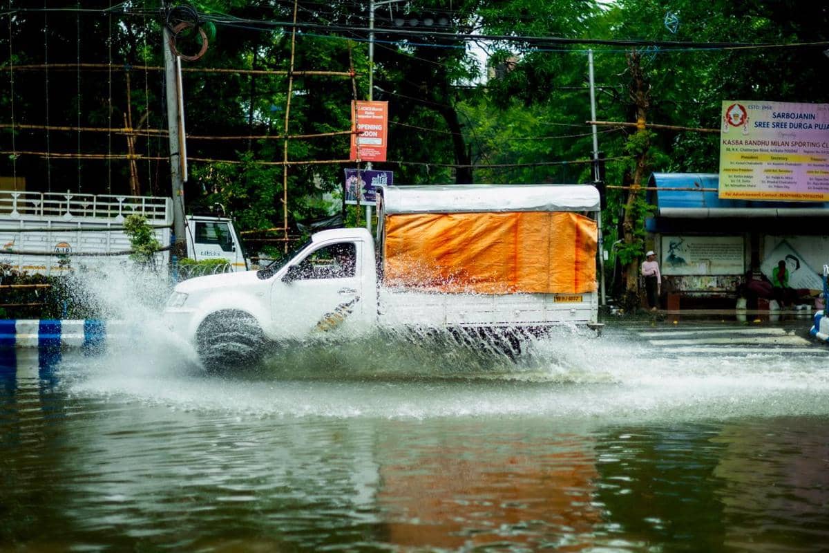 Sebuah truk melaju di jalan basah dengan permukaan aspal memantulkan cahaya dan suasana perjalanan yang lembap.