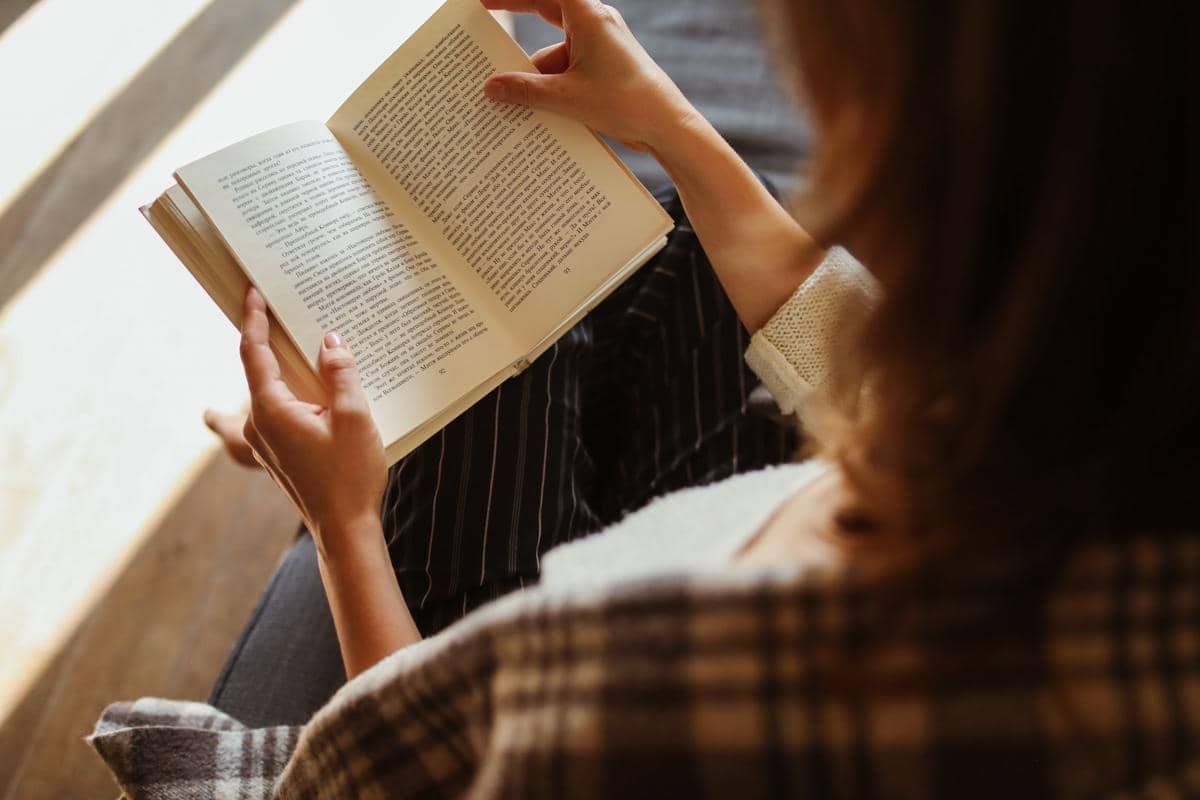 Seorang wanita menikmati kegiatan membaca buku sembari bersantai di dalam ruangan, mengabadikan momen kenyamanan dan waktu senggang.