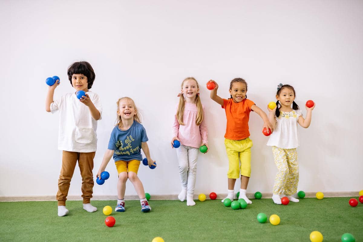 Sejumlah anak bermain bersama bola-bola warna-warni di dalam ruangan, menciptakan suasana ceria dan aktif.