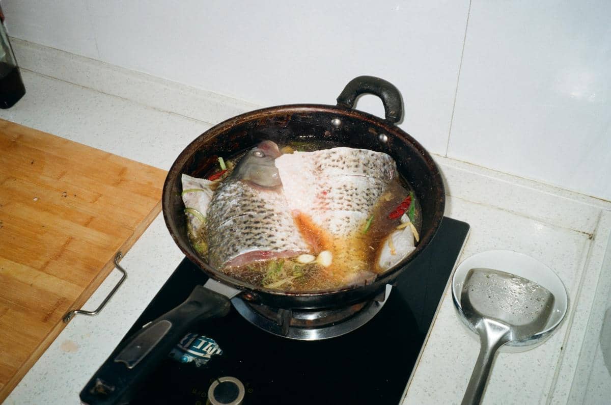 Ilustrasi proses membuat gulai ikan tenggiri dengan bahan dan bumbu masakan tradisional di atas meja dapur.