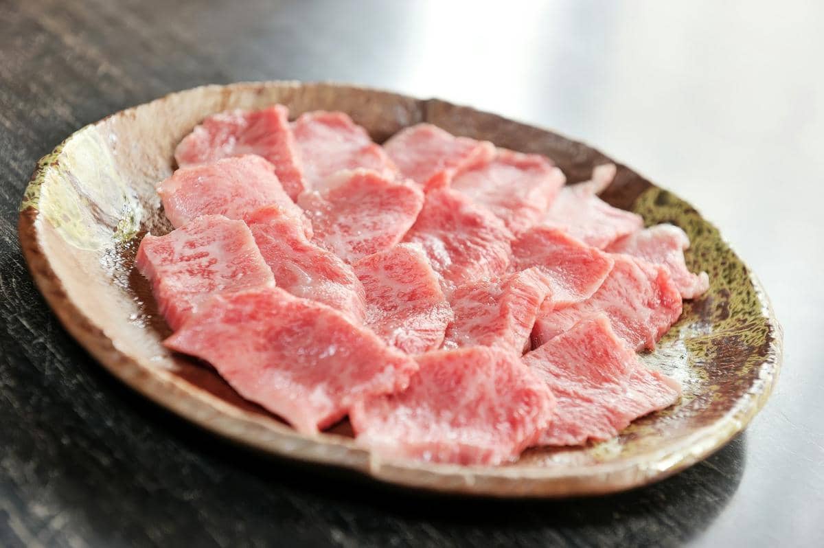 Potongan daging sapi mentah berwarna merah di atas talenan kayu untuk ilustrasi soegogi gamja guk Korea.