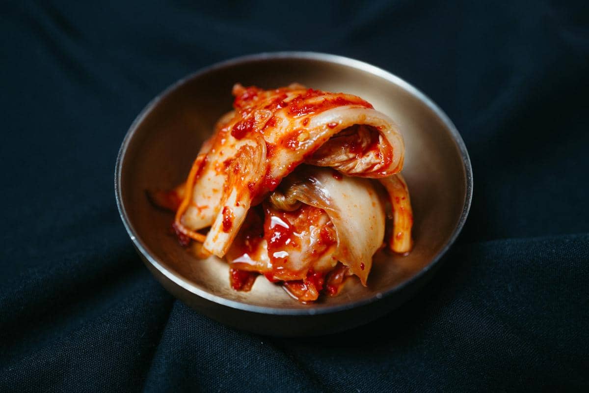 Ilustrasi kimchi, hidangan sayuran fermentasi khas Korea berwarna merah-oranye yang disajikan dalam wadah.