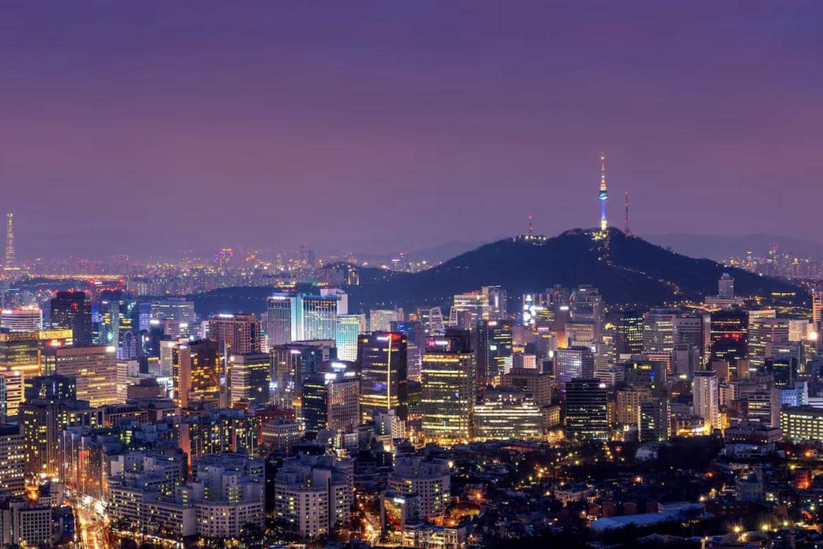 Panorama kota Seoul pada malam hari dengan gedung-gedung tinggi, cahaya lampu perkotaan, dan langit gelap.
