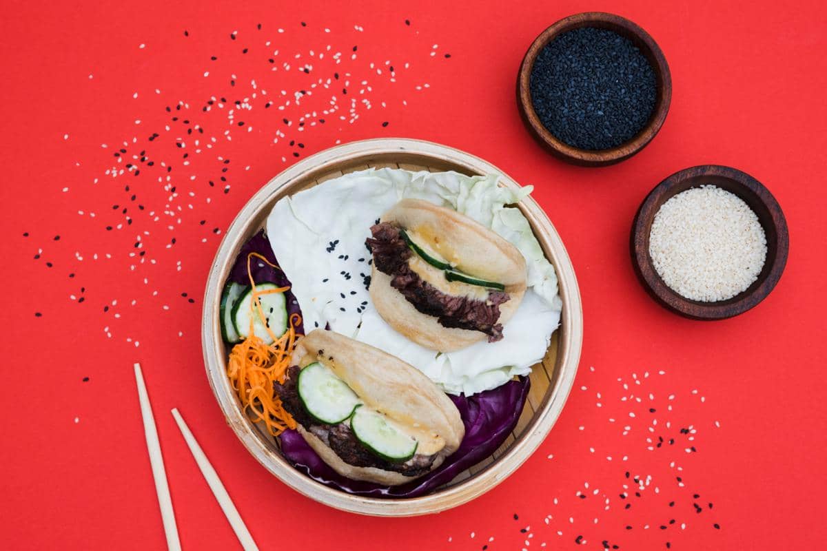 Ilustrasi gua bao berupa roti kukus lipat dengan isian, disajikan sebagai hidangan khas Asia dalam tampilan menggugah selera.