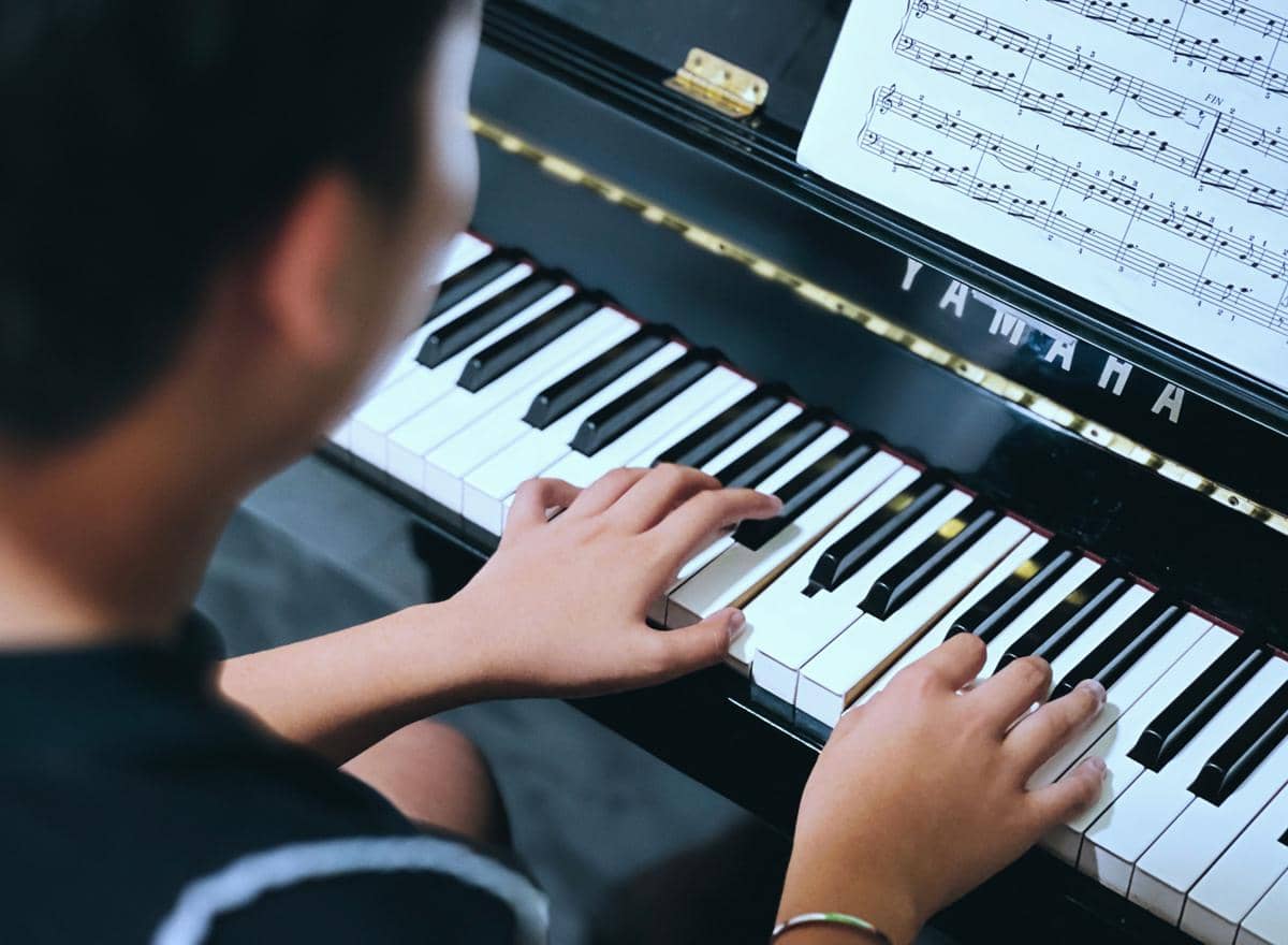 Ilustrasi seseorang bermain piano dengan tangan menekan tuts hitam dan putih pada alat musik tersebut.