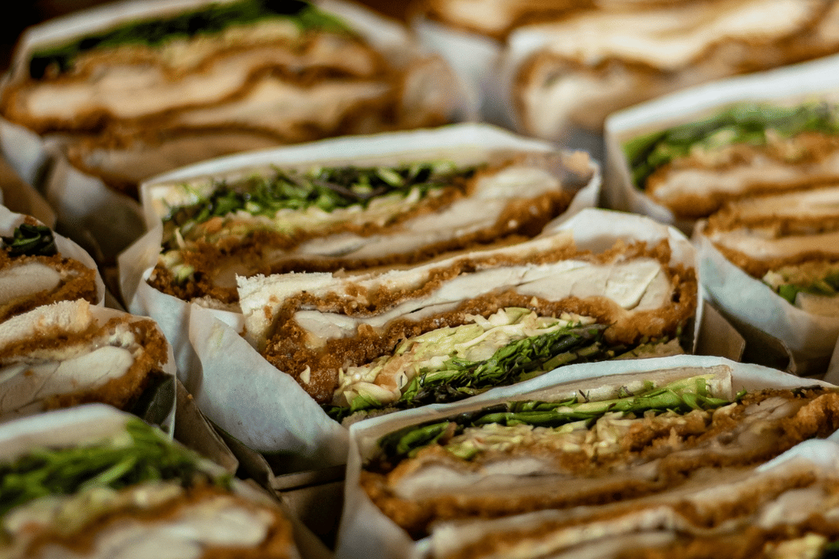 Sandwich ayam crispy berlapis pesto slaw dan sayuran segar, disajikan di atas piring sebagai ilustrasi makanan.