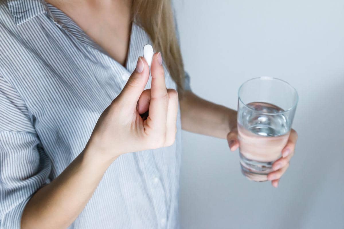 Segelas air putih dengan pil dan kemasan obat di atas meja sebagai ilustrasi kebiasaan minum obat secara rutin.