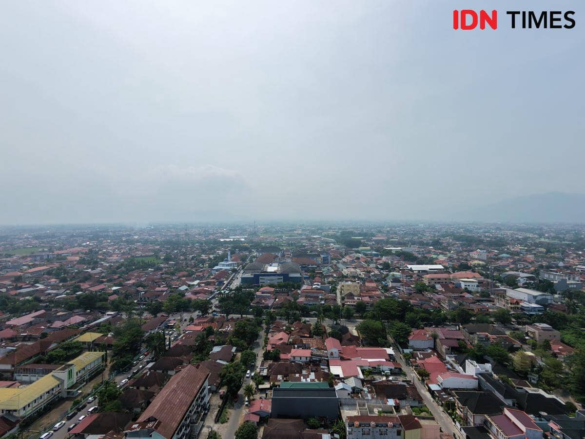 Pemandangan udara Kota Padang dengan bangunan, jalan, dan pepohonan yang tampak samar tertutup kabut asap.