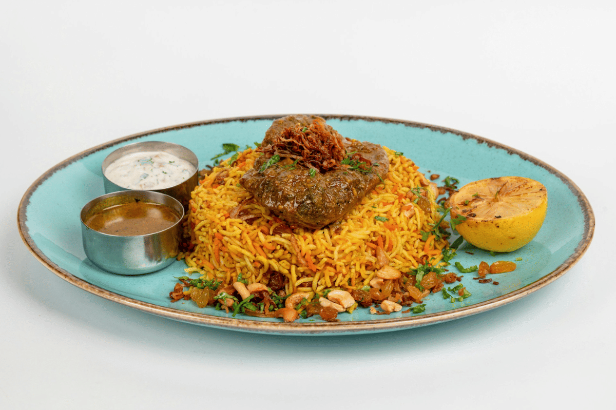 Ilustrasi nasi briyani dengan iga sapi berbumbu, disajikan bersama pelengkap dan rempah aromatik.