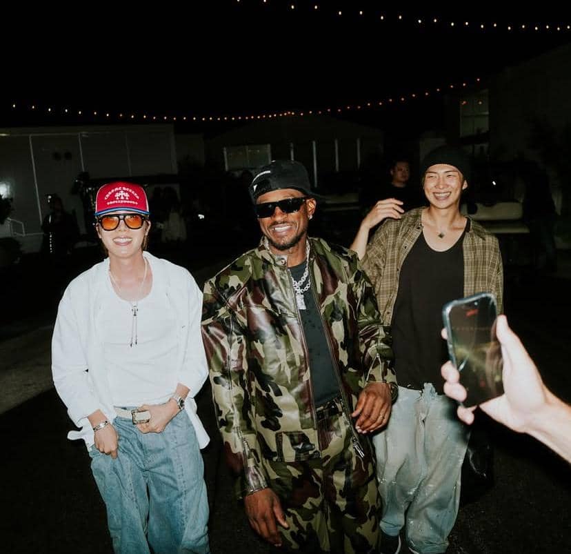 J-Hope dan RM BTS berpose bersama Usher dan Chris Brown saat menonton konser, tersenyum menghadap kamera.