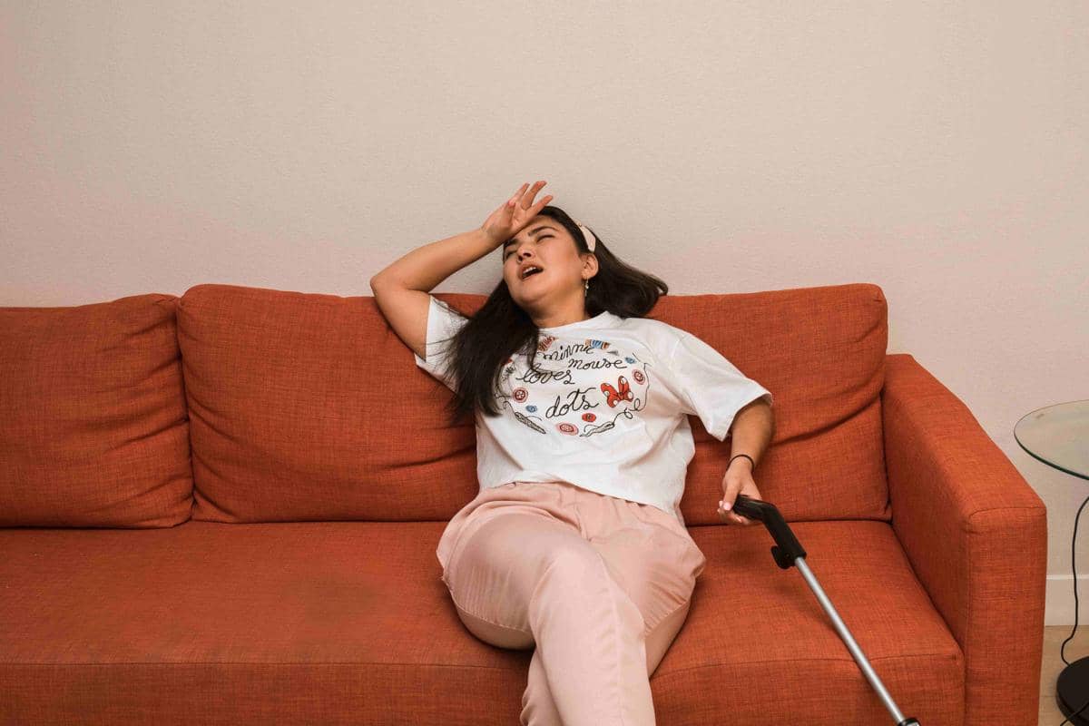Seorang perempuan duduk kelelahan di lantai dekat ember dan perlengkapan kebersihan setelah membersihkan rumah.