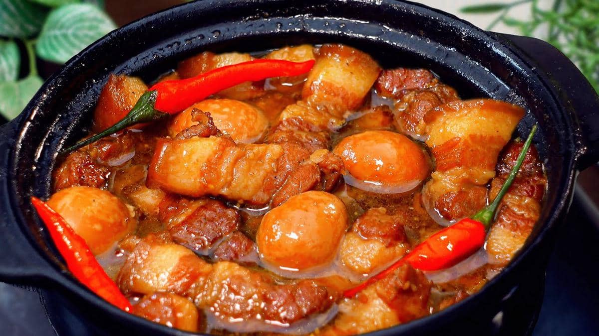 Ilustrasi thit kho tau berupa hidangan daging berwarna cokelat dengan telur rebus, disajikan dalam mangkuk putih.